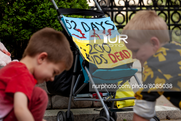 Two boys play in front of a sign affixed to a stroller counts the number of days the war in Ukraine has continued, as well as the number of...