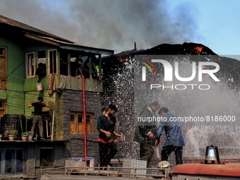 Locals and Fire services employees trying to douse a fire as People watch after several houses Gutted in Fire Incident in Baramulla, Jammu a...