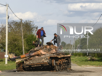 Local men explore burned tank on the street in Zahaltsi village near Kyiv, Ukraine, ​May 13, 2022. (