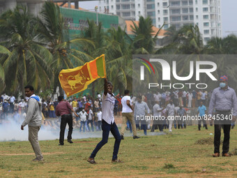A Sri Lankan pro-government protester runs with a Sri Lankan flag amid tear gas as they clash with anti-government protesters at Gotagogama...