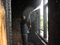 A Kashmiri man douses the fire at a  damaged residential house where two local militants were killed in the Gundipora area of south Kashmir'...