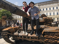 People pose for photography on a burned Russian tank displayed for Ukrainians to see at Mykhailivska Square in downtown Kyiv, Ukraine, June...