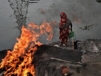 A woman searches for metal as a plastic cover of metal wire burns near the Buriganga River in Dhaka, Bangladesh on June 08, 2022. Buriganga...