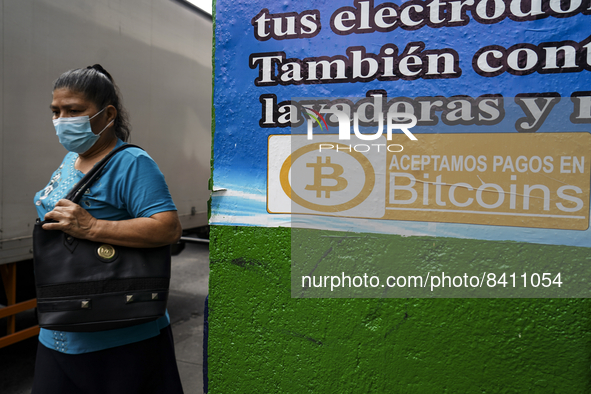 A woman walks next to a sign displaying the acceptance of Bitcoin as a payment method on June 15, 2022 in San Salvador, El Salvador. El Salv...