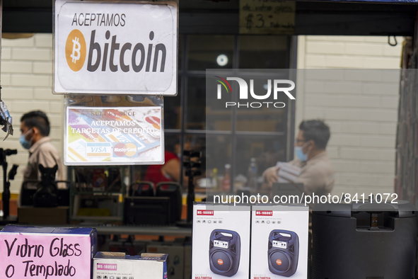People walk as a sign is displayed announcing the acceptance of Bitcoin as a payment method on June 15, 2022 in San Salvador, El Salvador. E...