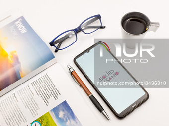 In this photo illustration a Squid Game logo seen displayed on a smartphone screen on a desk next to a cafe, a pen, glasses and a magazine i...