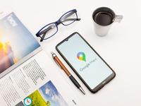In this photo illustration a Google Maps logo seen displayed on a smartphone screen on a desk next to a cafe, a pen, glasses and a magazine...