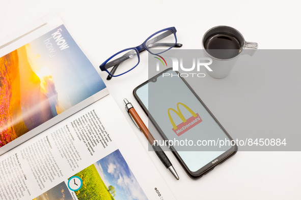 In this photo illustration a McDonald's logo seen displayed on a smartphone screen on a desk next to a cafe, a pen, glasses and a magazine i...