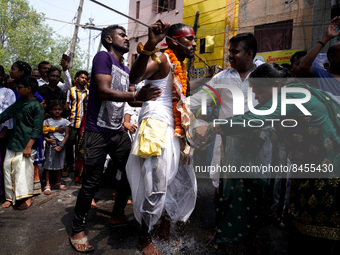 A woman performs rituals as a Hindu devotee with a metal skewer pierced through his mouth takes part in a Hindu religious procession to mark...