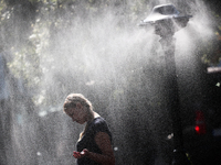 A woman cools herself by by a water sprinkler installed in the city during the heat wave in Krakow, Poland on July 21, 2022. (