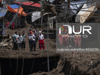 Members of the Iranian Red Crescent Society (IRCC) and firefighters (R) stand on an area which is demolished and covered with mud in flash f...