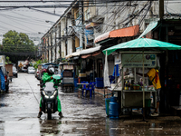 A GrabFood Delivery driver adjusts a green mobile phone umbrella next to a street food vendor with a large green umbrella. Daily life during...