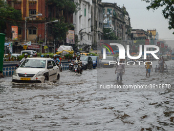 Commuters and cars are seen making their way through a flooded road after heavy rain in Kolkata , India , on 2 August 2022 . (