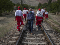 Members of the Iranian Red Crescent Society (IRCC) walk along a railway in the flooded village of Mazdaran in Firoozkooh county 124 km (77 m...
