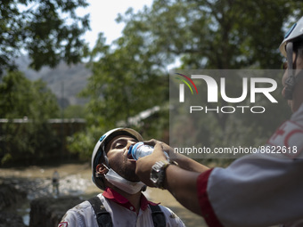 A member of the Iranian Red Crescent Society (IRCC) helps his colleague to drink water as they prepare to search for a body of a flood victi...