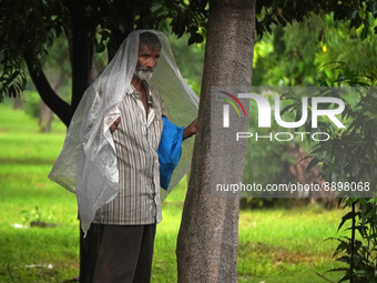 A man covers himself with a plastic sheet as he stands under a tree during a spell of rain in New Delhi, India on September 22, 2022. (