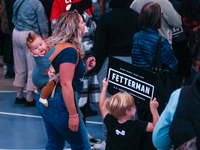 A mom with her infant on her back stands with her older son holding a campaign sign for John Fetterman during a rally for Fetterman in NW Ph...