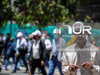 A street vendor wears a Gustavo Petro campaign cap as anti-government protesters march behind during the first antigovernment protest agains...
