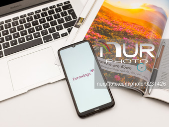 In this photo illustration an Eurowings airlines logo seen displayed on a smartphone screen on a desk next to a Macbook and atravel magazine...