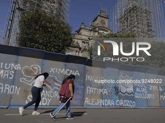 Two women walk in Mexico City's Zócalo in front of metal fences with slogans on the occasion of the International Day for the Elimination of...
