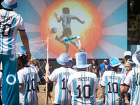An image of  Diego Armando Maradona is seen on a screen as people wearing Lionel Messi shirts attend a Fan Fest to watch the match between A...