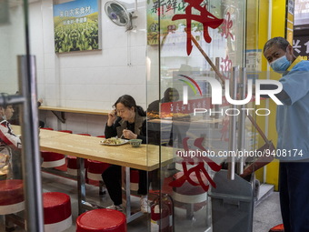 A women eating in a restaurant while a cleaner is working outside on January 8, 2023 in Shenzhen, China. China today lifts its requirement f...