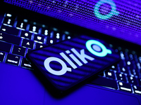 A binary code displayed on a laptop screen, a laptop keyboard and Qlik logo displayed on a phone screen are seen in this illustration photo...