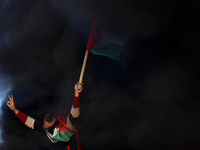 A Palestinian man holds a Palestinian flag during clashes with Israeli forces, near the Israel-Gaza border east of Gaza City, January 26, 20...