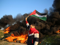 A Palestinian man holds a Palestinian flag during clashes with Israeli forces, near the Israel-Gaza border east of Gaza City, January 26, 20...