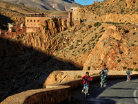 Boys ride bicycles along a road winding through the Dades Gorge in the Dades Valley deep in the High Atlas Mountains in Dades, Morocco, Afri...