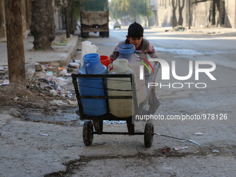 A Syrian boy pushes a cart with jerrycans filled with water in Aleppo on December 30, 2015 as residents of the northern city suffer constant...