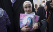 A young veiled Iranian girl looks on while holding her bag with a cartoon image of a veile...