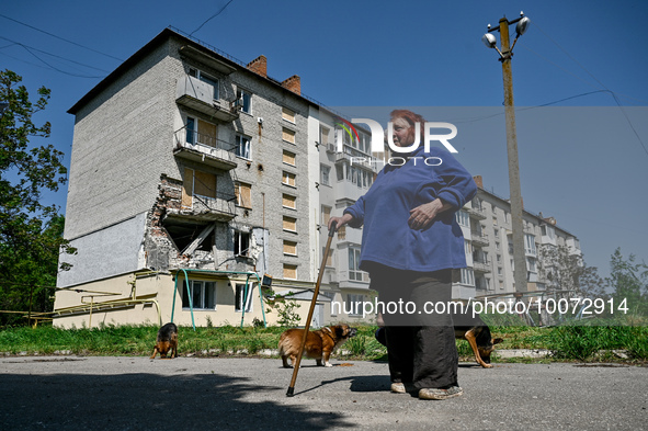 ZAPORIZHZHIA REGION, UKRAINE - MAY 18, 2023 - A local resident surrounded by stray dogs is seen outside a residential building damaged as s...