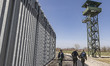 Border police walking alongside the fortification fence with a watch tower post in the bac...