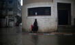 A Palestinian woman holds her son as she crosses a road flooded with rainwater following h...