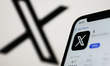 X on App Store displayed on a phone screen and X logo displayed on a screen in the backgro...