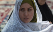 A veiled Iranian woman looks on as she sits at a holy shrine while taking part in a religi...