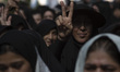 A veiled Iranian woman flashes a Victory sign as she stands at a holy shrine during a reli...