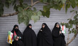 Veiled Iranian women holding Iranian flags and a Palestinian flag, stand on a side of a st...