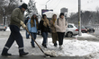A municipal worker is shoveling snow from the pavement while young women walk past in wint...