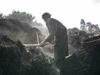 An Egyptian laborer is collecting charcoal from a pile in Al Bostan, Beheira Governorate, Egypt, on December 17, 2023.  (