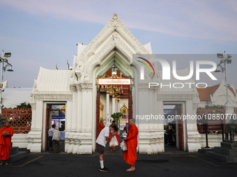 People are making merit by offering food to a Buddhist monk during the morning alms ahead of New Year's Eve outside Wat Benchamabopitr in Ba...