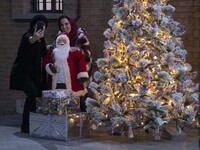 Two Iranian-Christian women are taking a selfie with a statue of Santa Claus while standing next to a Christmas tree at the Saint Targmancha...