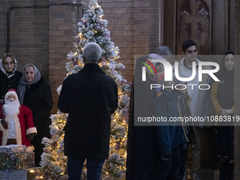 A veiled Iranian woman is standing next to a Christmas tree at the Saint Targmanchats Church in eastern Tehran with her relatives, during a...