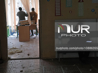 A boy is sitting on a bench in the corridor while men are holding a window frame inside a classroom at school N221, which was damaged in the...