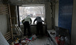 Two men are looking out of a knocked-out window in a residential building in the Solomians...