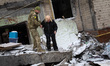 A serviceman is helping a woman walk over the rubble outside an apartment building in the...