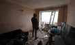 A man is standing in front of a broken window in the middle of a room that has been damage...