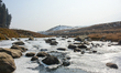 A partially frozen stream is flowing in Gulmarg, a ski destination, on a dry winter day in...