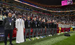 The substitutes and coach for Qatar are standing during the national anthems before the AF...
